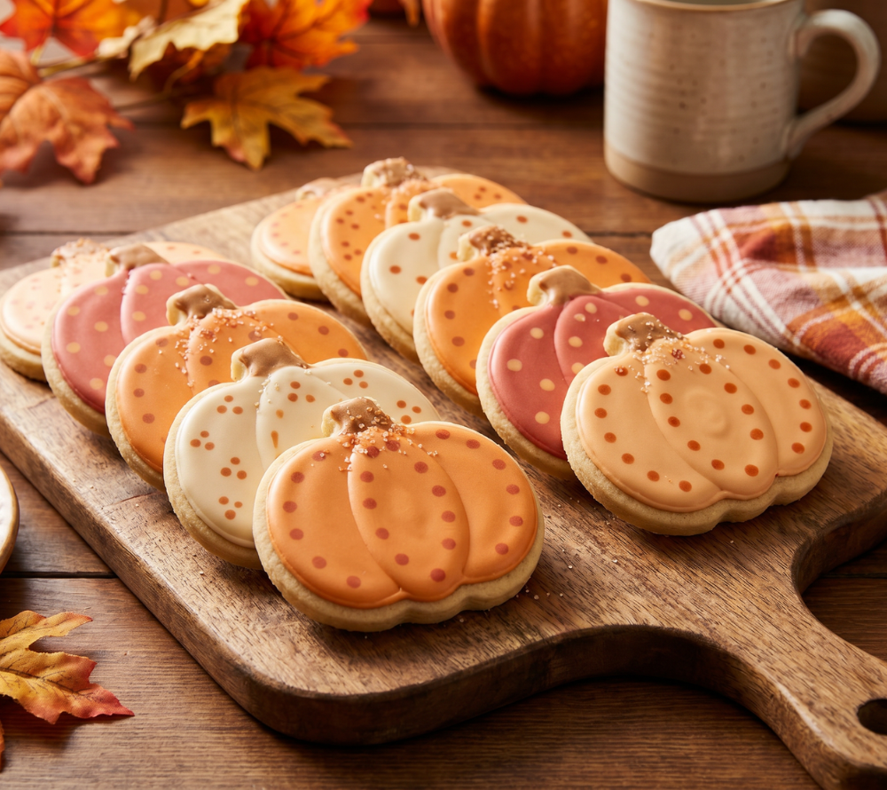 Kekse in Kürbisform dekoriert mit orange, beigen und braunem Zuckerguss liegen auf einem Holzbrett im Hintergrund ist herbstliche Deko